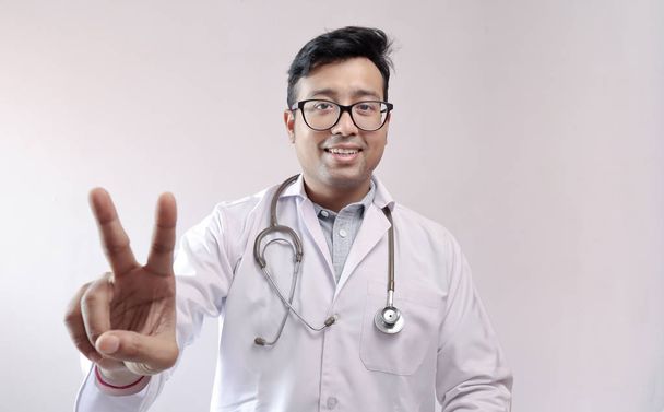 mužský indický lékař v bílém kabátě a stetoskop ukazující vítězné znamení důvěry - Fotografie, Obrázek