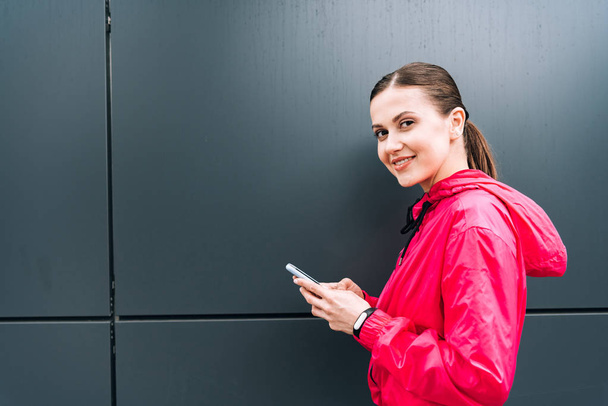 улыбающаяся привлекательная молодая женщина, держащая смартфон на улице
 - Фото, изображение