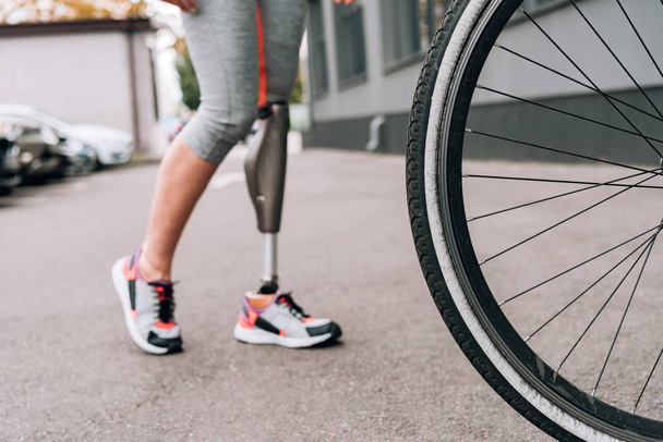 partial view of disabled sportswoman with prosthesis and bicycle on street - Фото, зображення