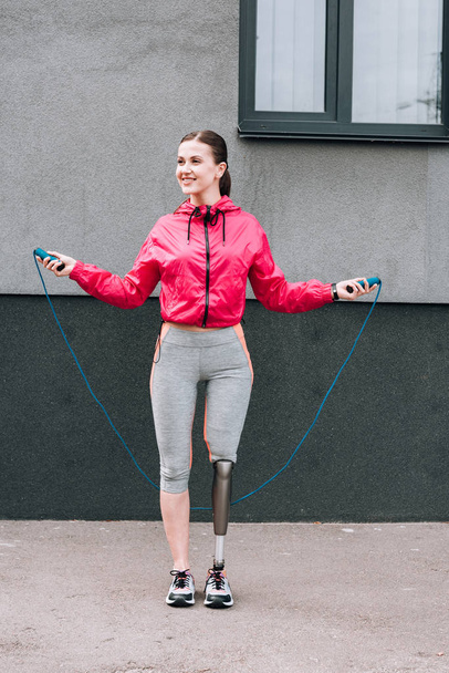 full length view of smiling disabled sportswoman with skipping rope on street - Foto, imagen