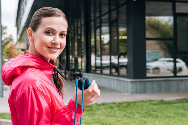 smiling attractive sportswoman holding skipping rope on street - Photo, Image