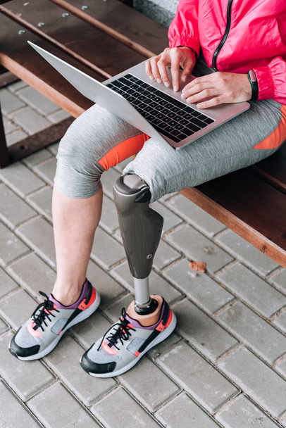 partial view of disabled sportswoman typing on laptop on street - Foto, afbeelding