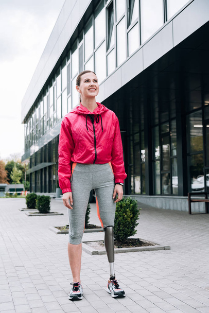 full length view of smiling disabled sportswoman with prosthesis on street - Photo, image