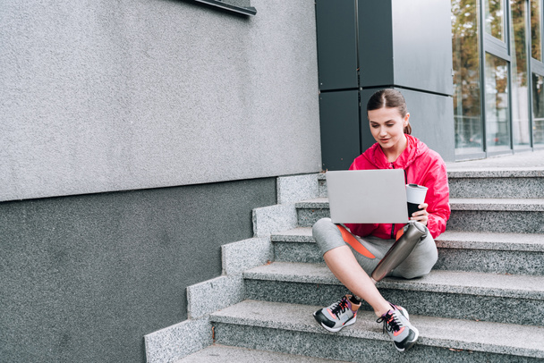 disabled sportswoman using laptop while sitting on stairs on street - Fotoğraf, Görsel