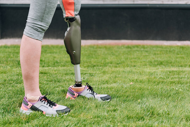 partial view of disabled sportswoman standing on grass on street - 写真・画像