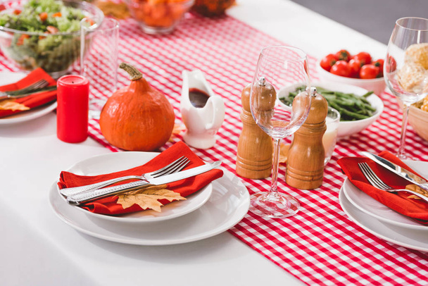 asztal tányérokkal, poharakkal, gyertyákkal, evőeszközökkel, borsdarálóval, sómalommal és sütőtökkel Hálaadás napján  - Fotó, kép