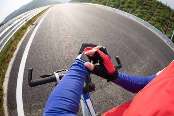 Woman cyclist set the smartwatch before riding bike on highway - Zdjęcie, obraz