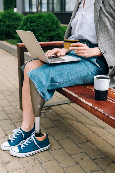 partial view of disabled woman with laptop sitting on bench and holding credit card - Fotó, kép