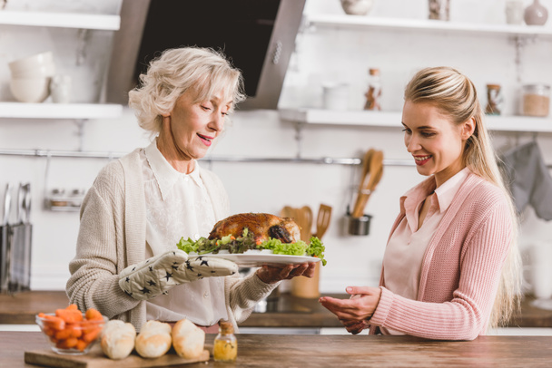 smiling mother and daughter holding plate with tasty turkey in Thanksgiving day  - Foto, Imagem
