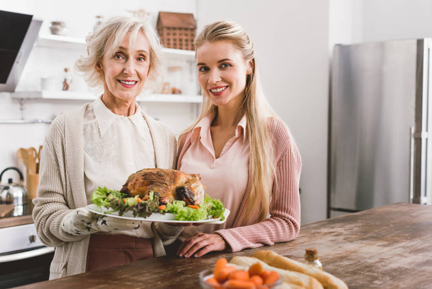smiling mother and daughter holding plate with tasty turkey in Thanksgiving day  - Foto, immagini