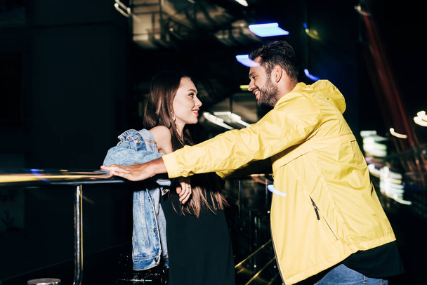 side view of smiling boyfriend and girlfriend looking at each other in night city   - Фото, изображение