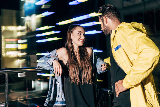 smiling girlfriend and boyfriend talking and looking at each other in night city  - Фото, изображение