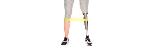panoramic shot of disabled sportswoman with prosthetic leg training with resistance band isolated on white - 写真・画像