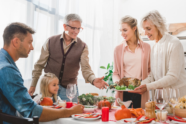  μέλη της οικογένειας κάθονται στο τραπέζι και κρατώντας πιάτο με γαλοπούλα την ημέρα των Ευχαριστιών       - Φωτογραφία, εικόνα