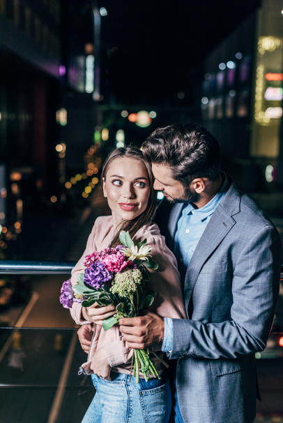 handsome businessman giving bouquet and hugging attractive woman in night city  - Fotó, kép