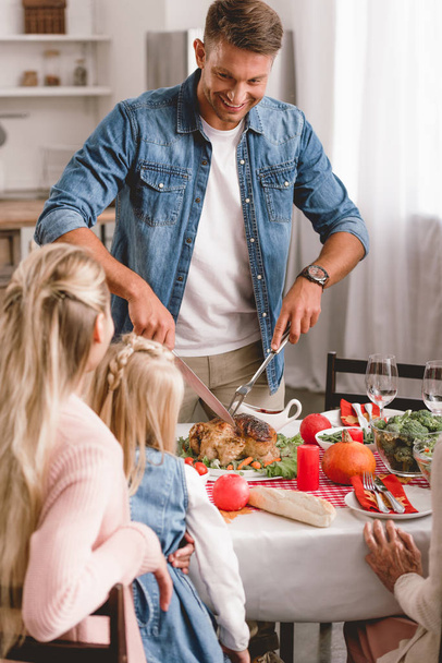 valikoiva painopiste perheenjäsenten istuu pöydässä ja isä leikkaa maukasta kalkkunaa kiitospäivänä
       - Valokuva, kuva