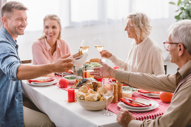 smiling family members sitting at table and clinking with wine glasses in Thanksgiving day    - Photo, Image