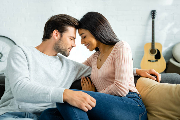 vista lateral da mulher americana africana e homem bonito com os olhos fechados sorrindo e abraçando no apartamento
  - Foto, Imagem