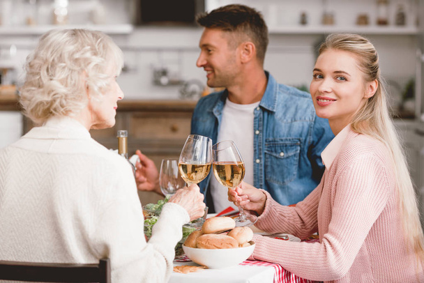 улыбающиеся члены семьи, сидящие за столом и звенящие с бокалами вина в День Благодарения
    - Фото, изображение