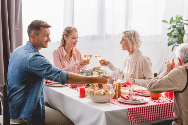 sorridente familiari seduti a tavola e clinking con bicchieri di vino nel giorno del Ringraziamento
    - Foto, immagini