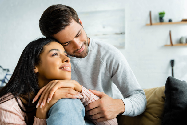 african american woman and handsome man smiling and hugging in apartment  - Foto, imagen