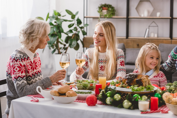 μέλη της οικογένειας κάθονται στο τραπέζι και κρατώντας ποτήρια κρασιού τα Χριστούγεννα  - Φωτογραφία, εικόνα