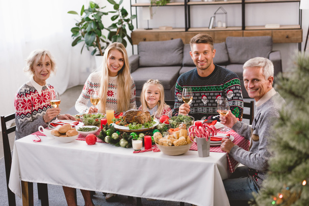 smiling family members sitting at table and holding wine glasses in Christmas  - Foto, afbeelding