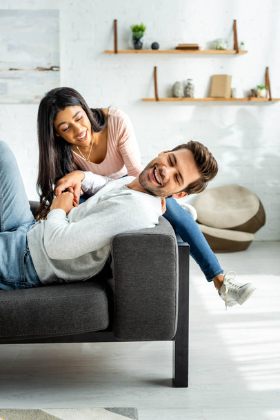 african american woman and handsome man smiling and sitting on sofa in apartment  - Foto, imagen