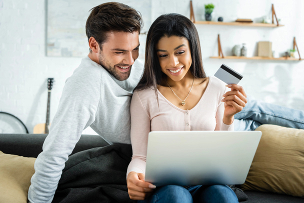 african american woman holding credit card and looking at laptop with man  - Fotoğraf, Görsel