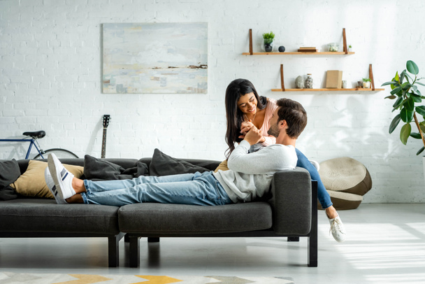 african american woman and handsome man smiling and sitting on sofa in apartment  - Foto, Bild
