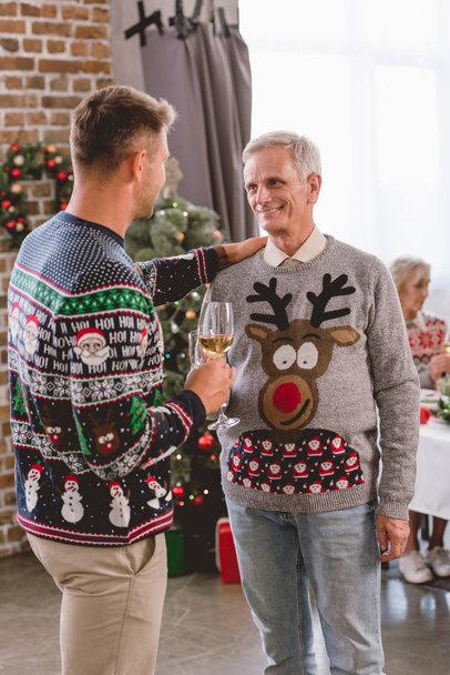 father and smiling grandfather holding wine glasses and talking in Christmas  - Fotó, kép