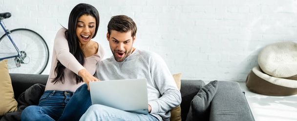 panoramic shot of shocked african american woman and handsome man pointing with finger at laptop  - Photo, Image