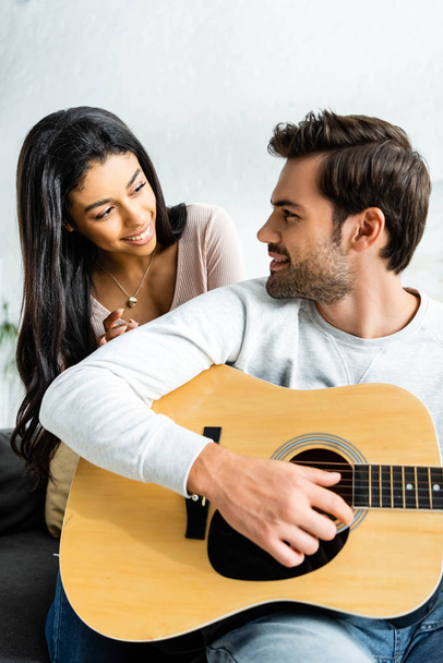 smiling african american woman looking at man with acoustic guitar - Foto, Bild