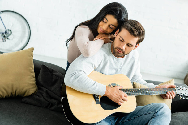 african american woman hugging handsome man with acoustic guitar - Photo, Image