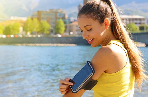 Opaska sportowa na smartfon. Sportowa dziewczyna dotykając jej inteligentnego telefonu przed treningiem fitness na plaży. - Zdjęcie, obraz