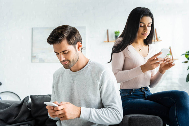 handsome man and african american woman sitting on sofa and using smartphones  - Fotó, kép