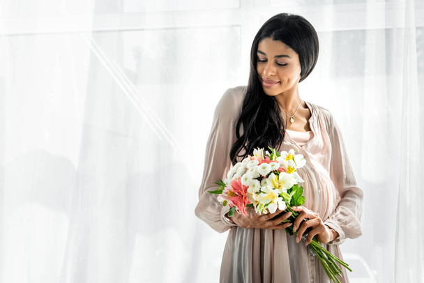 smiling pregnant african american woman holding bouquet in apartment - Photo, image