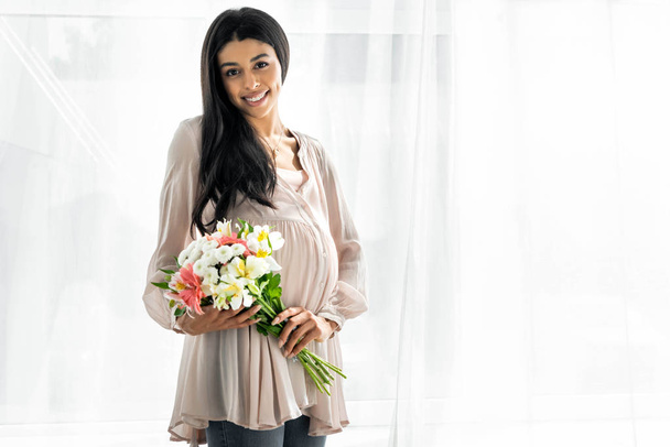 smiling pregnant african american woman holding bouquet in apartment - Photo, Image