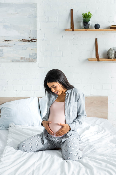 african american pregnant woman in pajamas smiling and hugging belly  - Photo, Image