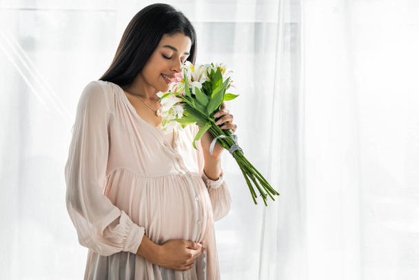 african american pregnant woman hugging belly and smelling bouquet  - Fotó, kép