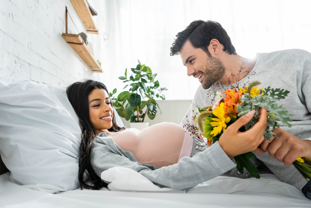 handsome man holding bouquet and looking at his pregnant african american woman  - Foto, afbeelding