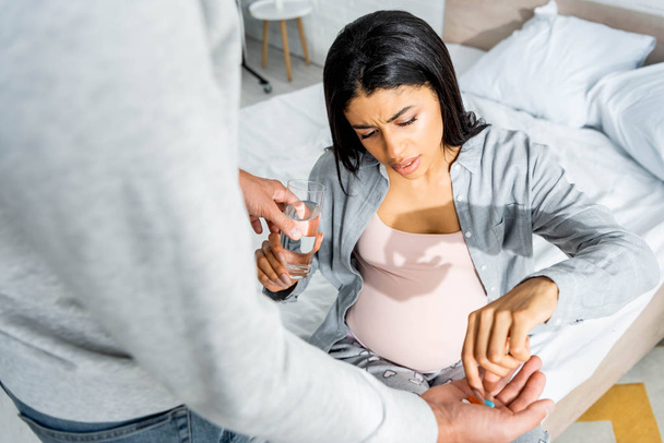 cropped view of man giving pills and glass of water to pregnant african american woman  - Foto, Imagem