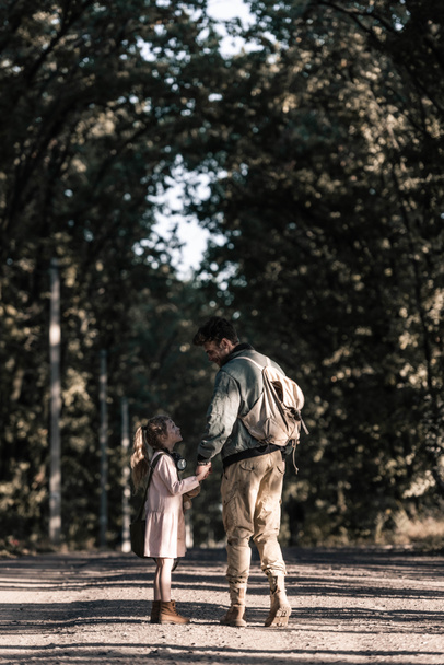 man holding hands with kid while standing on road, post apocalyptic concept - Foto, immagini
