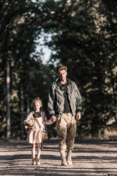 cute kid holding hands with man while holding teddy bear, post apocalyptic concept - Fotografie, Obrázek