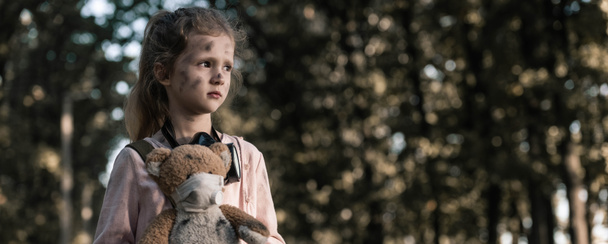 panoramic shot of kid holding dirty teddy bear near trees in chernobyl, post apocalyptic concept - Photo, Image