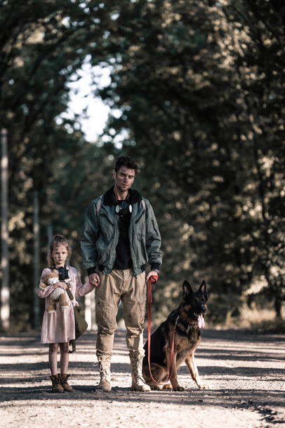handsome man holding hands with kid near german shepherd dog, post apocalyptic concept - Photo, Image