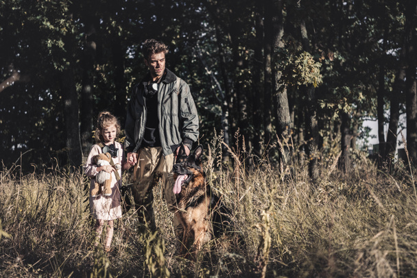 handsome man standing in field with kid and german shepherd dog, post apocalyptic concept - Photo, Image