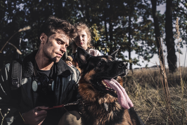 селективное внимание красивого мужчины, держащего на поводке немецкую овчарку рядом с ребенком, постапокалиптическая концепция
 - Фото, изображение