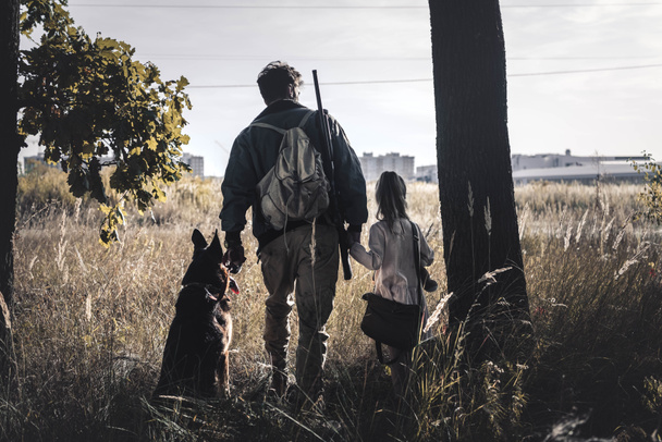 back view man standing in field with kid and german shepherd dog, post apocalyptic concept - Photo, Image