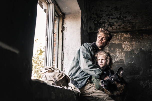 hombre abrazando chico sucio cerca perro pastor alemán en edificio abandonado, concepto post apocalíptico
 - Foto, Imagen